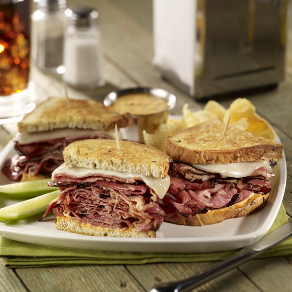 Sourdough pastrami melt sandwich on a plate with pickle spears