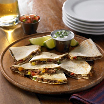 Shredded beef quesadillas on a plate with sour cream and lime wedges