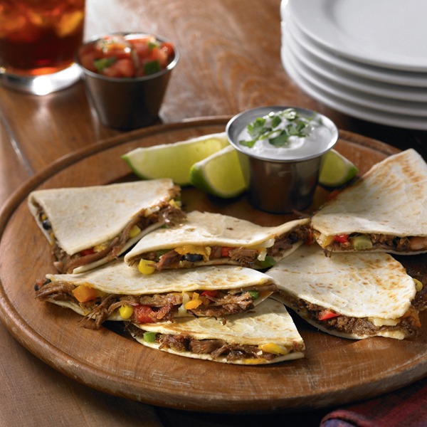 Shredded beef quesadillas with sour cream and lime wedges on a plate