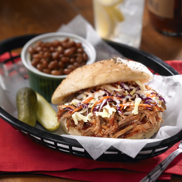 Carolina shredded pork and coleslaw sandwich in a basket with pickles and baked beans