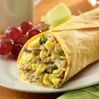 Carnitas breakfast burrito on a plate with grapes and melon