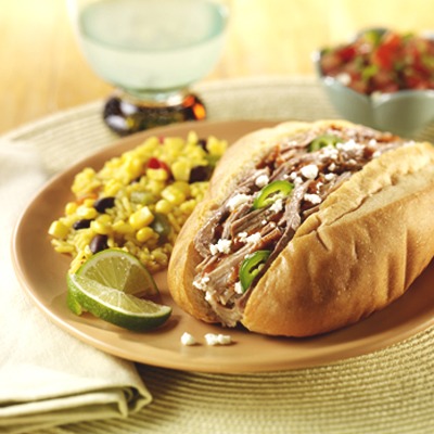 Shredded pork Mexican torta on a plate with corn and lime wedges