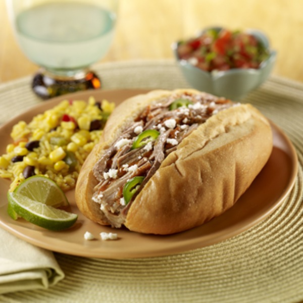 Shredded pork Mexican torta style sandwich on a plate with corn and lime wedges