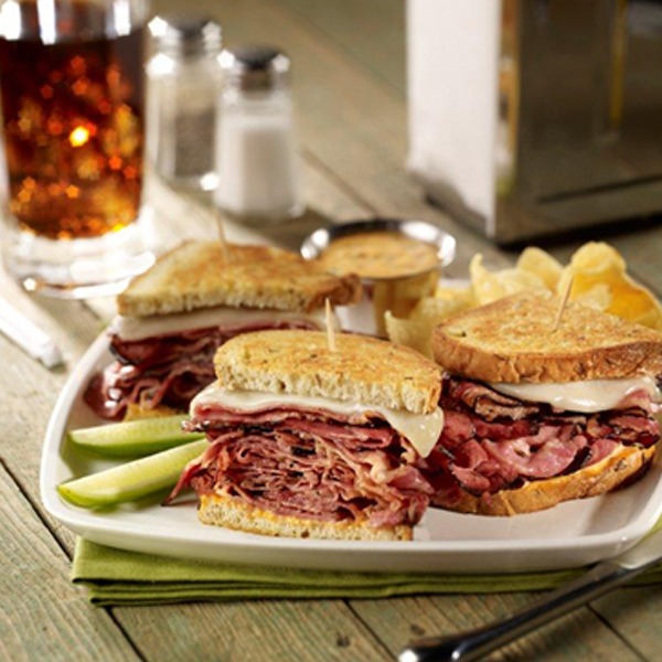 Sourdough sliced pastrami melt sandwich on a plate with pickle spears and potato chips