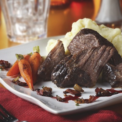 Braised pot roast bacon onion relish, carrots, and mashed potatoes on a plate