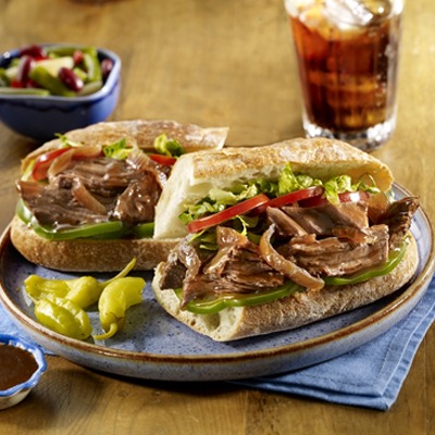 Pot roast po' boy on a plate with peppers and a glass of soda