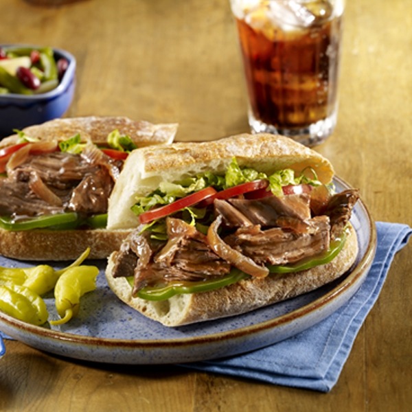 Pot roast po' boy on a plate with peppers and a glass of soda