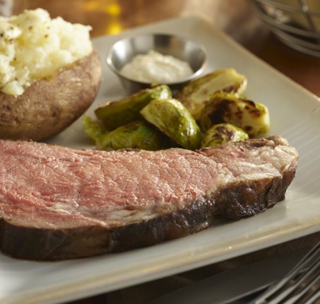 Prime rib with baked potato and brussel sprouts on a plate