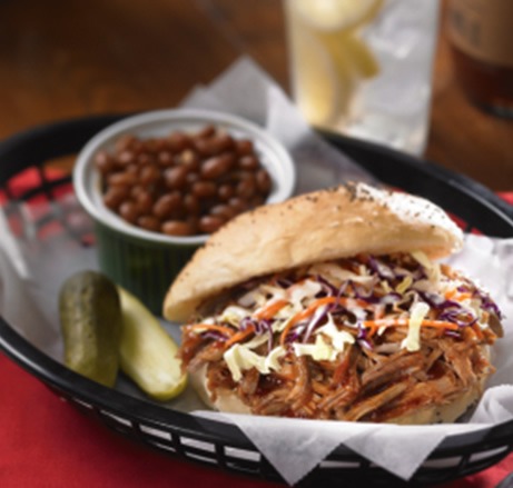 Carolina shredded pork and coleslaw sandwich in a basket with pickles and baked beans