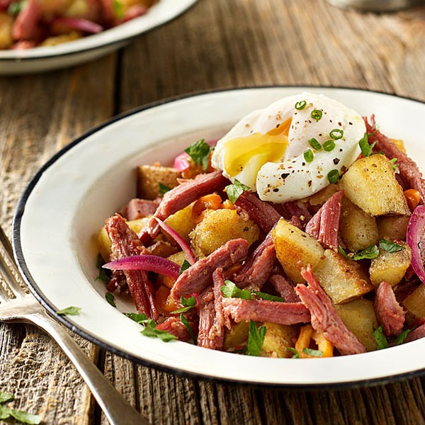 Corned beef hash in a bowl with potatoes, eggs, and pickled red onion